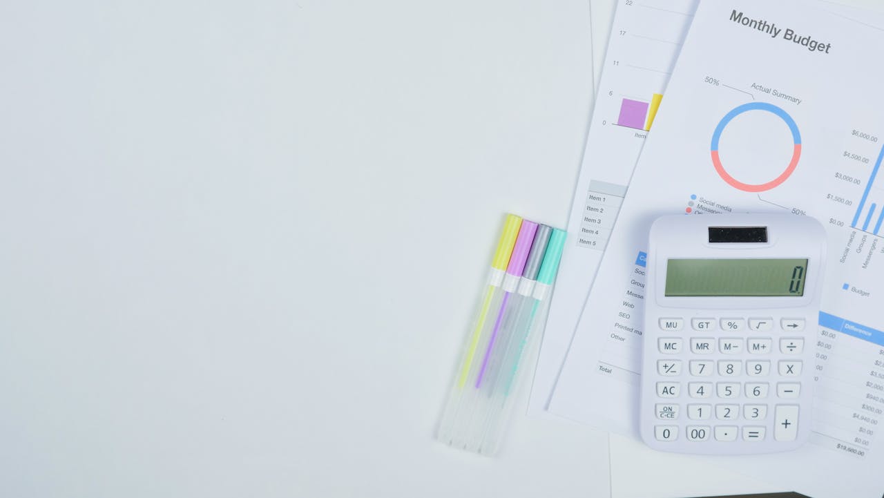 Minimalist office desk with a calculator, budget planning documents, and colorful pens.